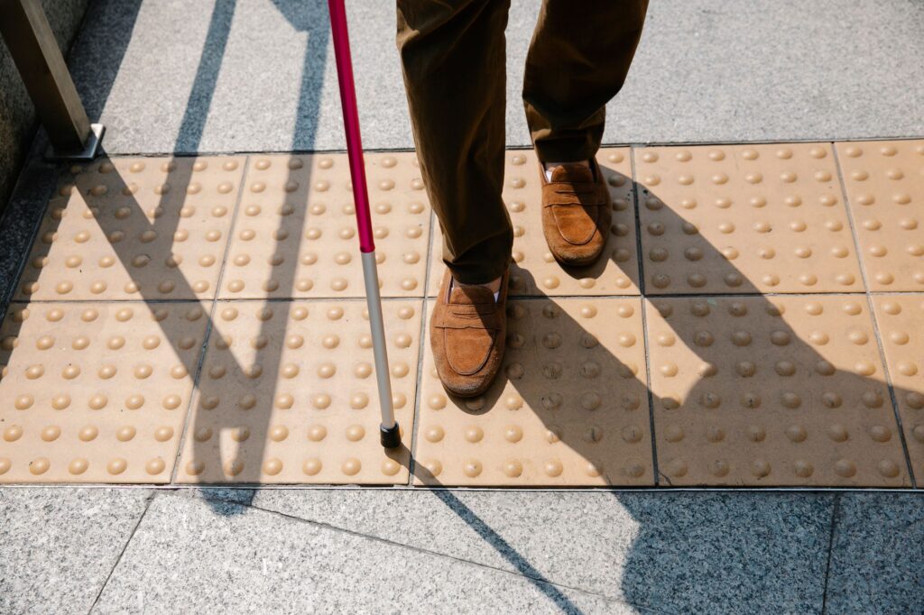 Close-up of a blind person walking on tactile paving with a cane, emphasizing accessibility.