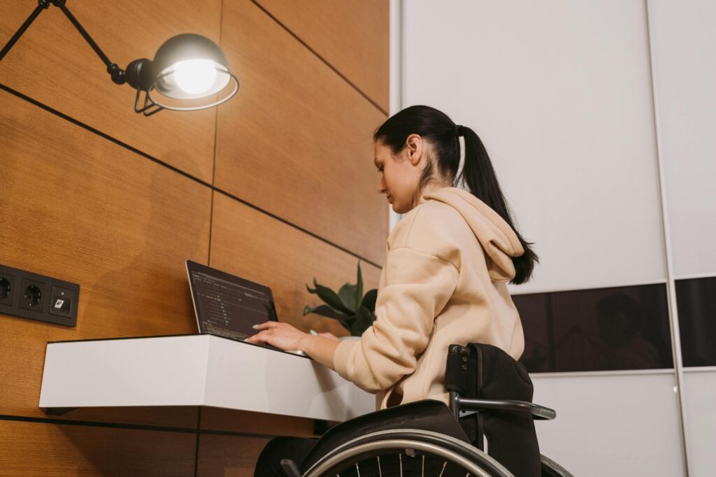 A woman in a wheelchair working on a laptop in a modern interior setting.