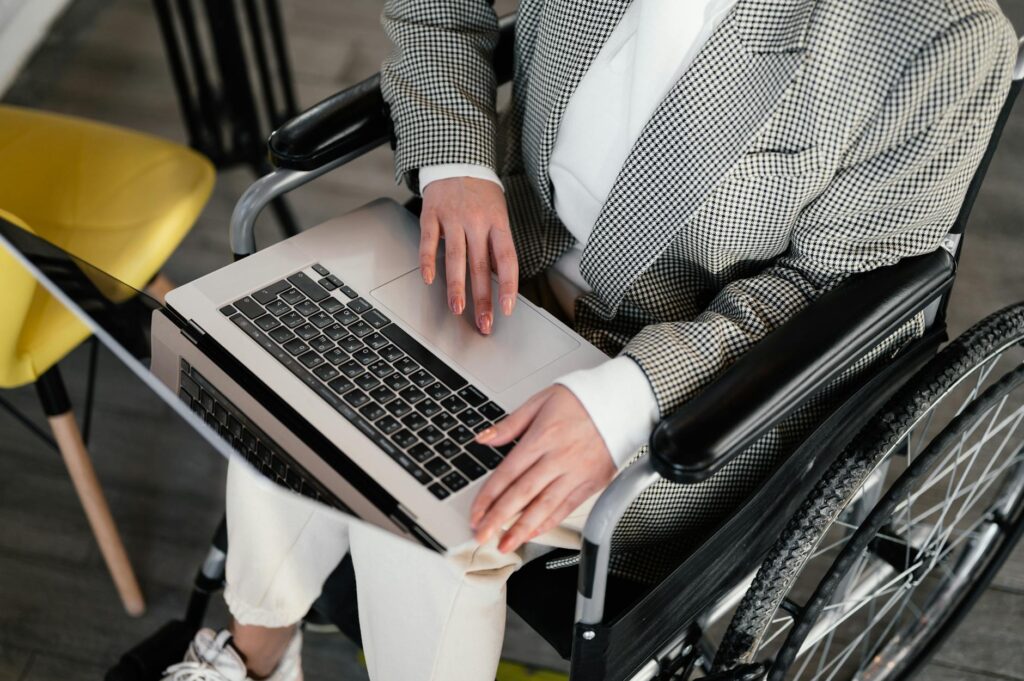 From above of unrecognizable female freelancer wearing elegant wear in wheelchair browsing internet on modern netbook while working in modern cafeteria