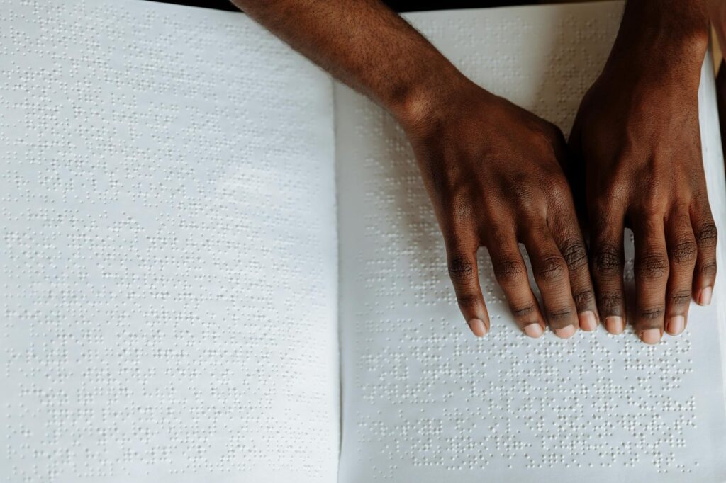 Close-up of hands reading a Braille book, highlighting tactile sensory perception for the visually impaired.